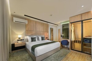 A hotel room with a bed, bedside table, lamp, wardrobe, and a mirror.