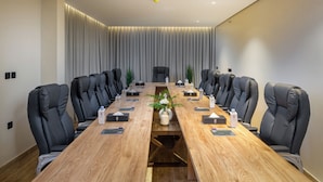 A conference room with a long wooden table, black leather chairs, and a central plant. - Aryash hotel  (Abha)