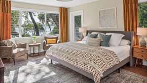 A bedroom with a large bed, two bedside tables, a chair, a small table with a plant, and a window with curtains. - Private Beach + Outdoor Oasis: Home in St Pete! (St. Petersburg)