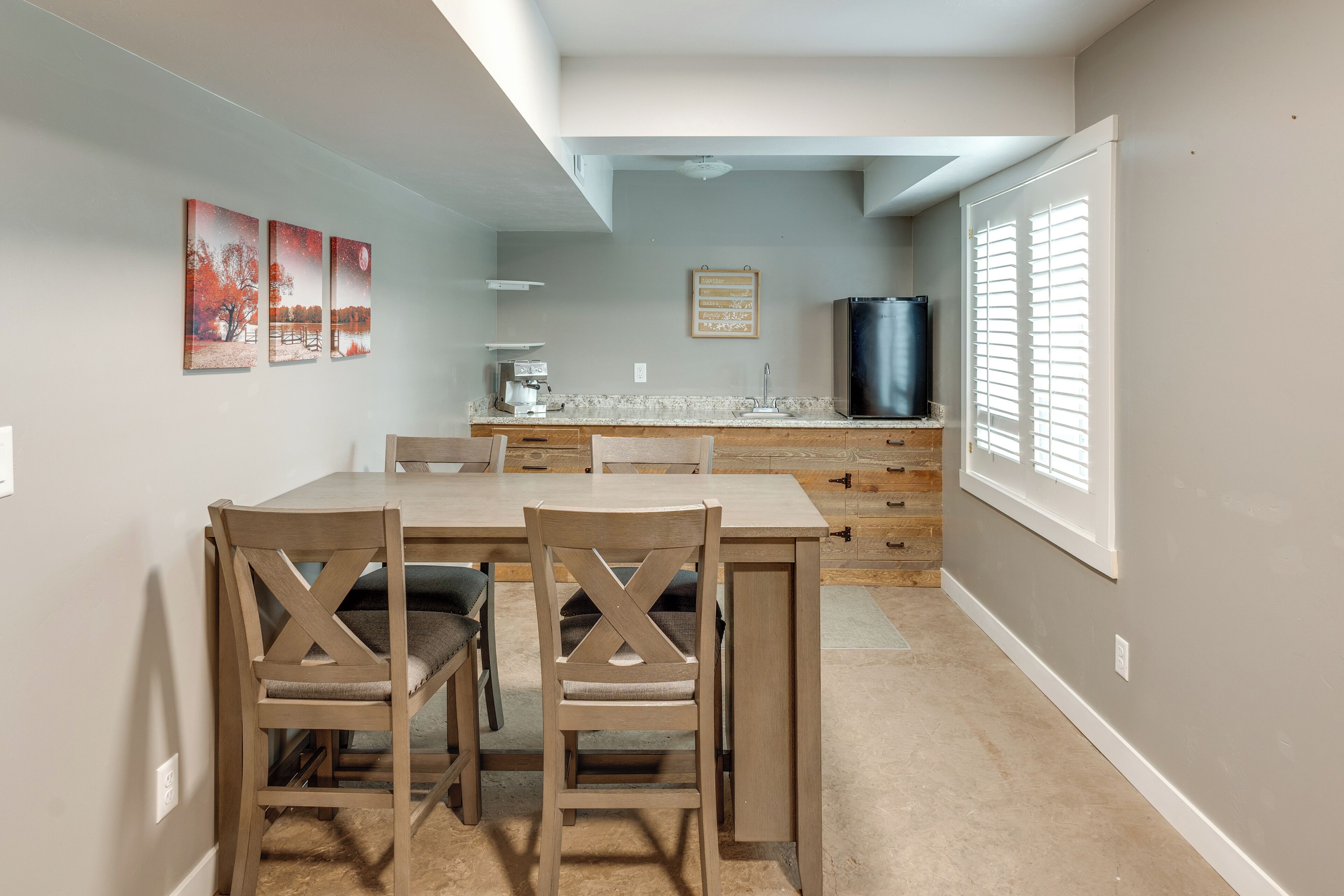 A dining area with a wooden table and chairs, a kitchen with a refrigerator, and a window with blinds.