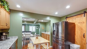A modern kitchen with wooden cabinets, a stainless steel refrigerator, and a dining area with a wooden table and chairs.