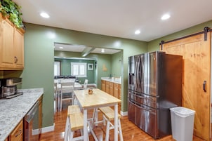 Una cocina moderna con armarios de madera, un refrigerador de acero inoxidable y un comedor con mesa y sillas de madera.