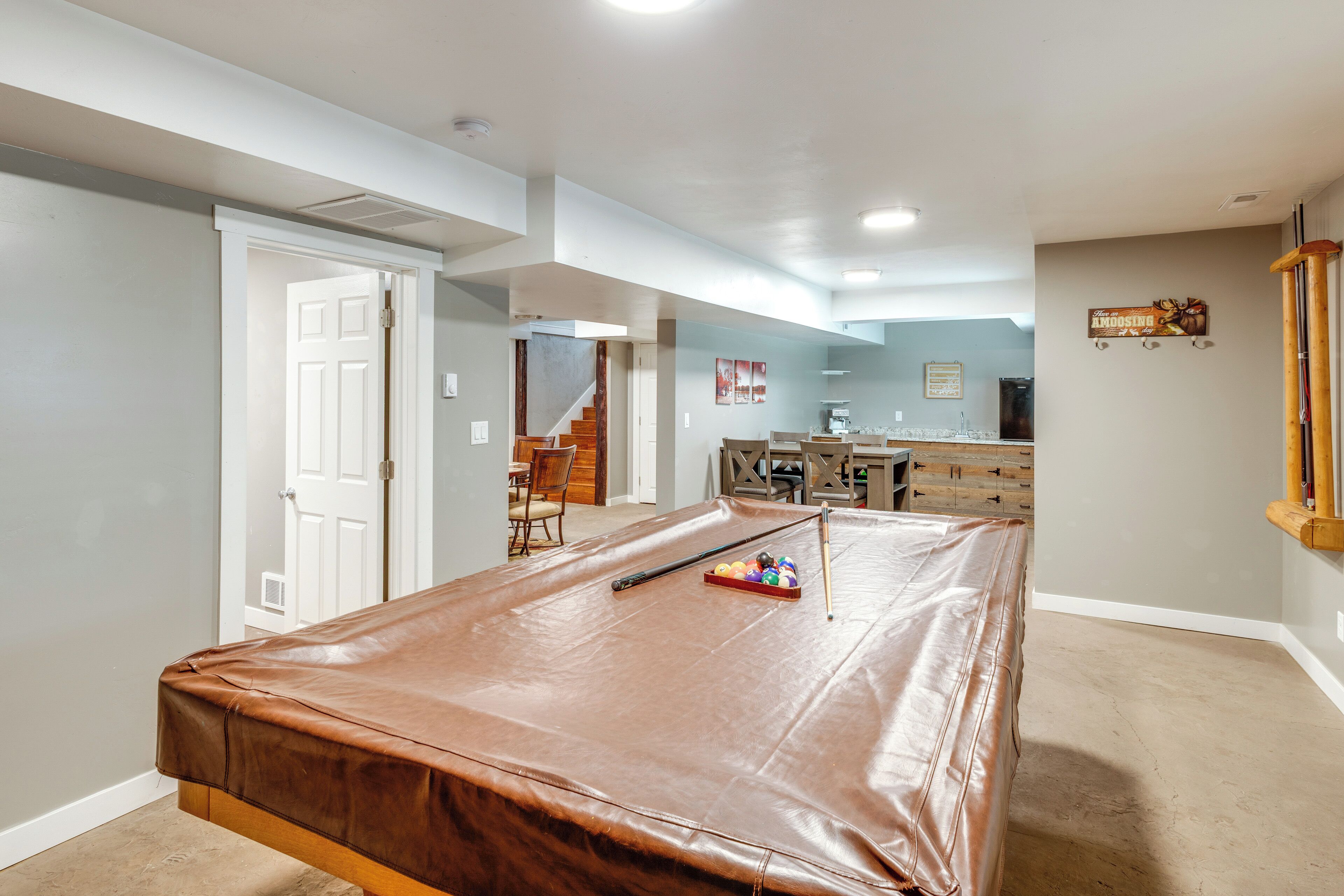 A spacious room with a pool table, a dining area, and a kitchen in the background.