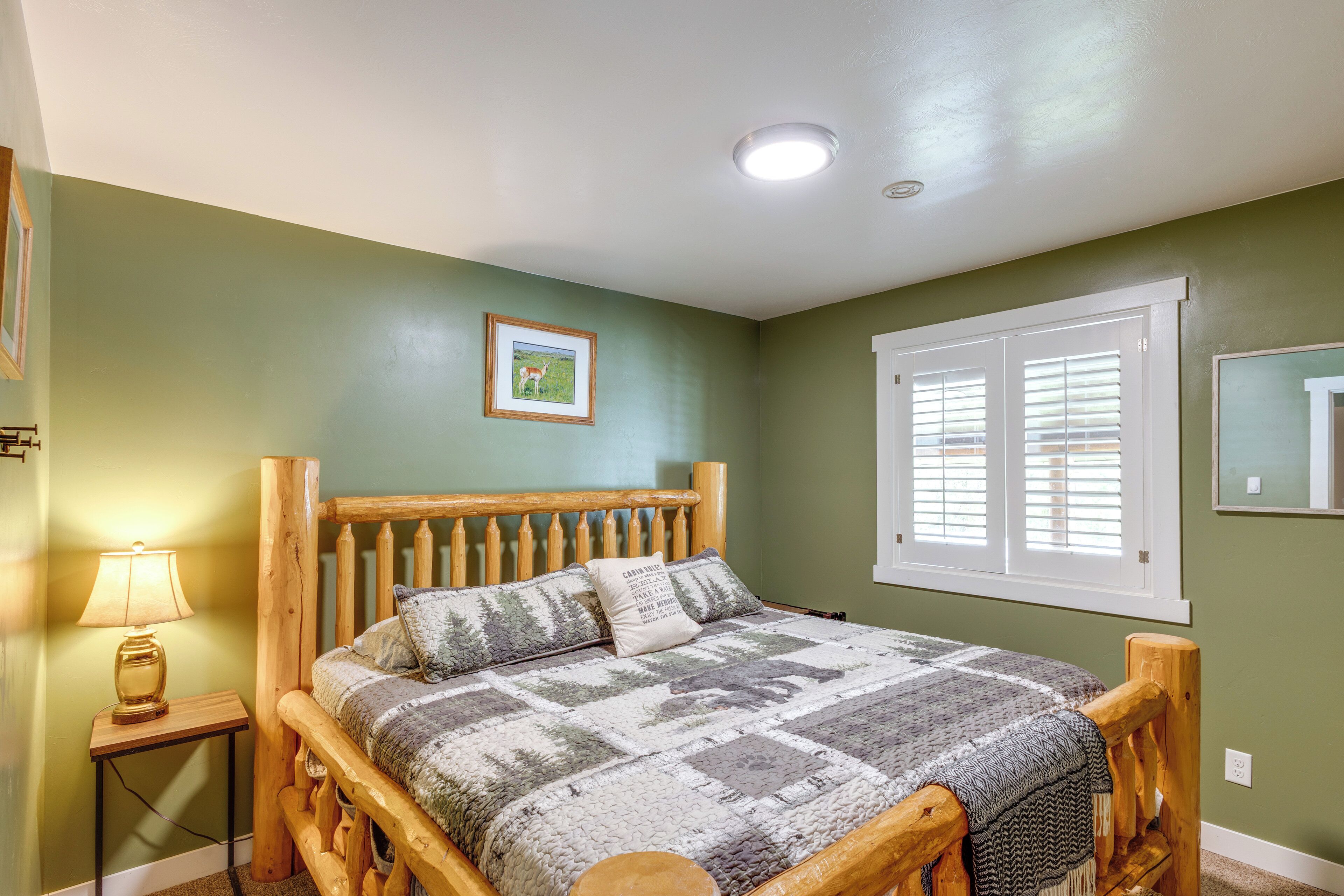 Une chambre à coucher avec un lit en bois, une table de chevet avec une lampe, un tableau encadré au mur et une fenêtre avec des stores.