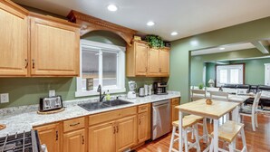 A kitchen with wooden cabinets, a sink, a stove, and a dining area with a table and chairs.