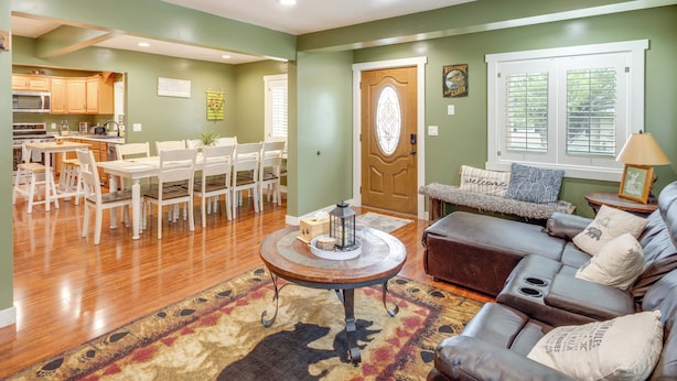 A spacious living room with a brown leather sofa, a dining area with white chairs, and a kitchen in the background.
