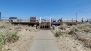 Un paseo marítimo en la playa con una puerta de madera, una barandilla de metal y un cielo despejado.