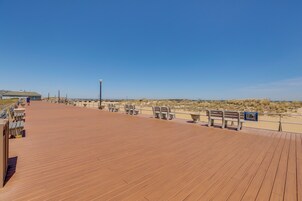 A wooden boardwalk with benches and a railing, overlooking a beach and dunes.