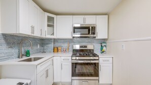 Una cocina compacta con armarios blancos, un microondas de acero inoxidable y un horno empotrado.
