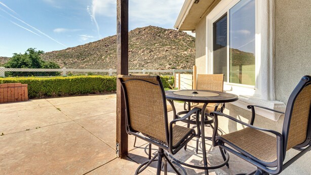 An outdoor patio with a table and chairs, a view of a mountain, and a building with large windows. - Family Hideaway w/ Hillside Views in Temecula! (Temecula)