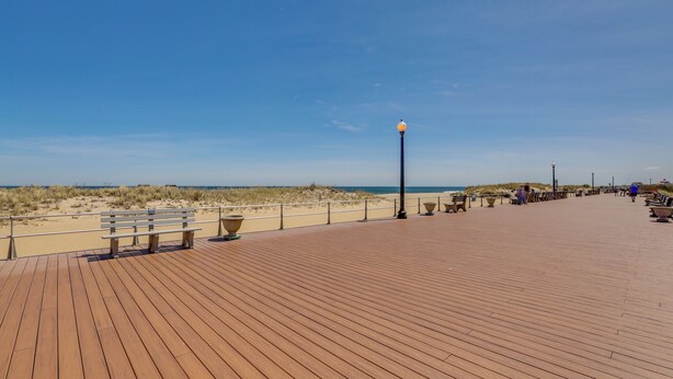 A wooden boardwalk with benches and potted plants, overlooking a beach with dunes. - Walk to Ocean Grove Beach: Apt in New Jersey (Ocean Grove)