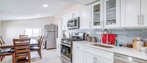 Una cocina moderna con armarios blancos, electrodomésticos de acero inoxidable y una zona de comedor con sillas de madera.