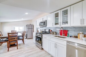 Una cocina moderna con armarios blancos, electrodomésticos de acero inoxidable y una zona de comedor con sillas de madera.