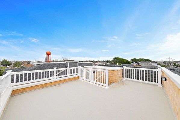 A rooftop terrace with white railings, a wooden deck, and a view of a distant water tower. - Steps From Sand & Fun: Beach Haven Retreat w/ Pool (Beach Haven)