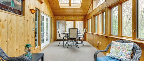 A wooden cabin interior with a dining area, two wicker chairs with blue cushions, a table with chairs, and a ceiling fan.