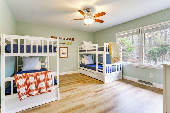 A room with bunk beds, a ceiling fan, and a window with a view of trees.