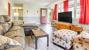 A living room with a leather sofa, ottoman, wooden coffee table, and a television on a wooden stand. - 1 Mi to Pisgah Natl Forest: Wooded Haven w/ Deck (Pisgah Forest)