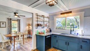 A kitchen with wooden flooring, a dining area with a table and chairs, a built-in dishwasher, and a window with a view of a house and trees. - Walk to River & Trails: Cozy Damascus Cottage! (Damascus)