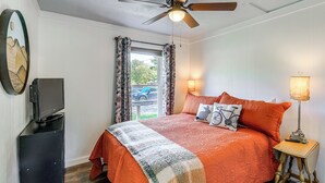 A bedroom with a bed, a ceiling fan, a TV on a stand, a lamp, and a window with curtains. - Walk to River & Trails: Cozy Damascus Cottage! (Damascus)