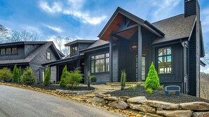 A modern two-story house with a dark exterior, large windows, and a stone foundation.