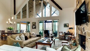 A spacious living room with a high ceiling, large windows, a stone fireplace, and a cozy seating area.