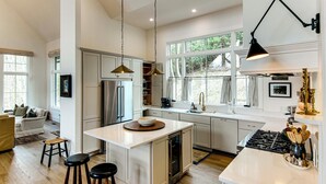 A modern kitchen with white cabinetry, a central island, stainless steel appliances, and large windows.