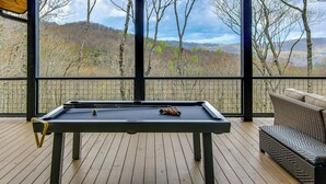 A pool table in a covered area with a view of a forested landscape.
