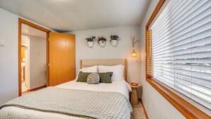 Een slaapkamer met een groot bed, een houten deur, een nachtkastje en een raam met jaloezieën.