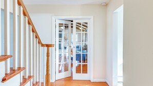 A staircase with wooden steps and white railings leading to a room with a large glass door. - Poconos Group Getaway w/ Game Room + Fire Pit! (Gouldsboro)