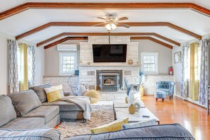 A spacious living room with a fireplace, a large TV, and a ceiling fan. - Poconos Group Getaway w/ Game Room + Fire Pit! (Gouldsboro)