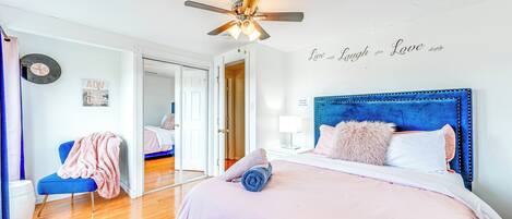 A bedroom with a bed, a ceiling fan, a chair, a nightstand, and a wall clock.