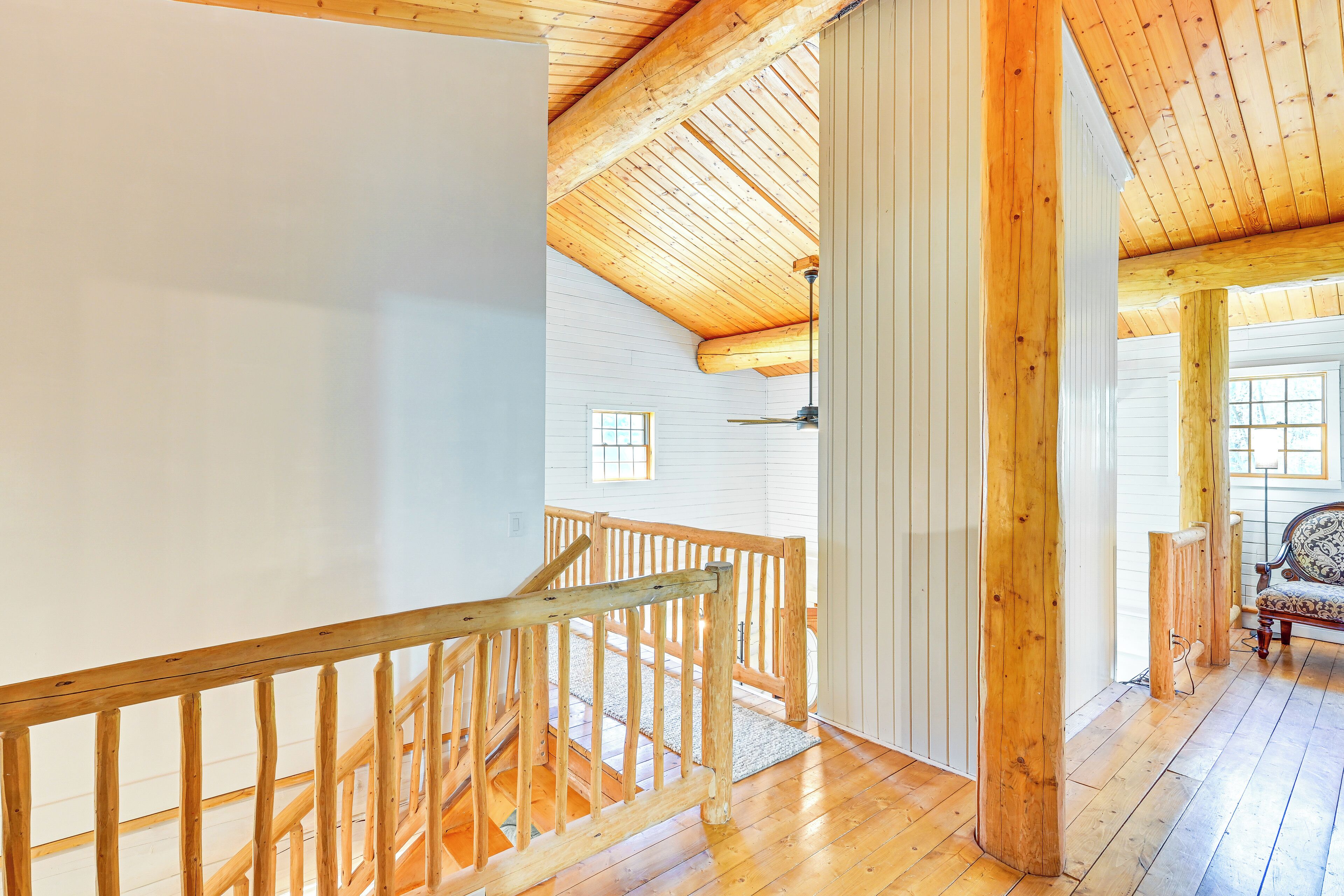 Un escalier en bois, doté d’une rampe, mène à une pièce aux murs blancs et au plafond en pente.
