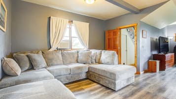 A living room with a sectional sofa, wooden flooring, a television, and a door leading to another room.