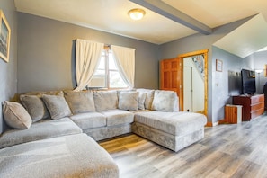 A living room with a sectional sofa, wooden flooring, a television, and a door leading to another room. - Algoma Lake Michigan Home w/ Game Room & Deck (Algoma)