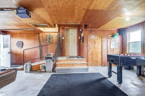 A wooden interior with a foosball table, a dartboard, and a staircase leading to a door. - Algoma Lake Michigan Home w/ Game Room & Deck (Algoma)