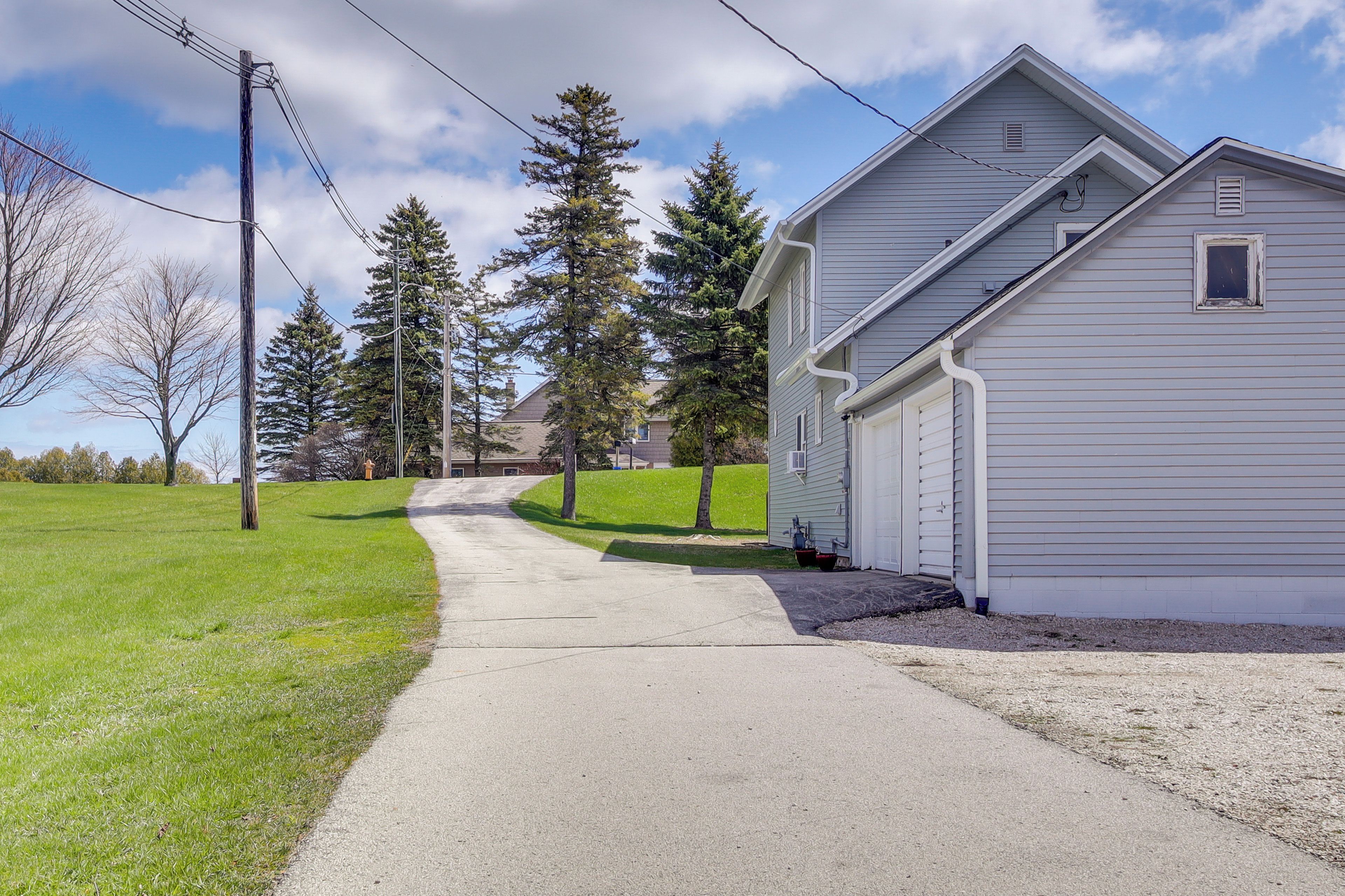 A residential driveway leading to a house with a garage, surrounded by trees and a grassy area.