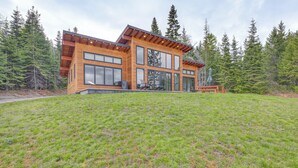 Eine moderne Blockhütte mit großen Fenstern, einer Terrasse und Wald im Hintergrund.