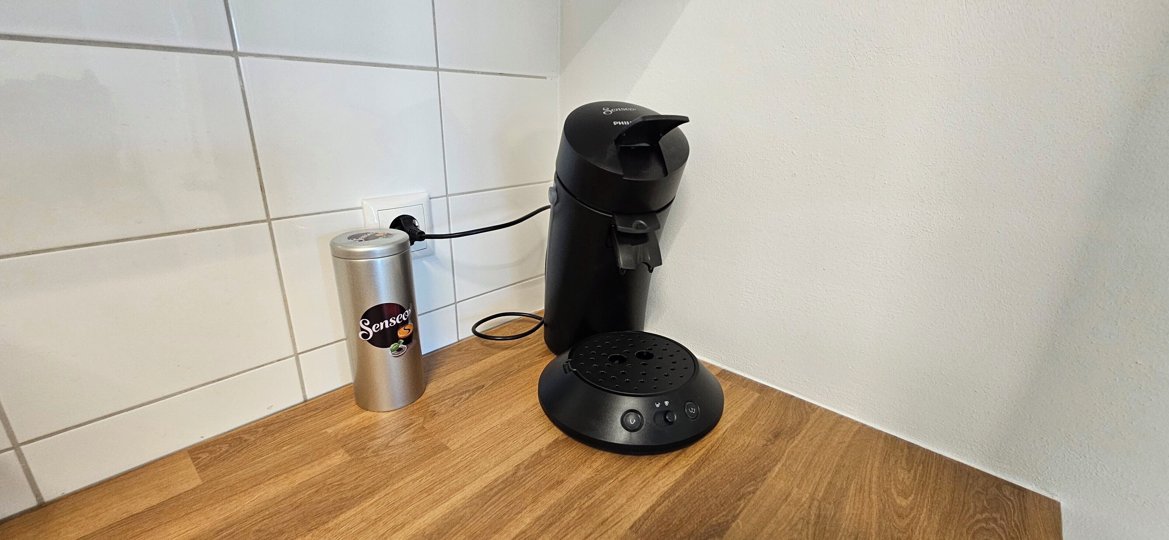 Eine schwarze Kaffeemaschine und eine silberne Dose auf einer Holzauskład.