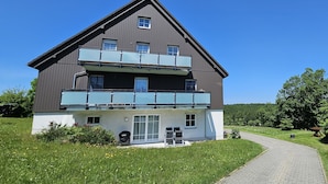 A two-story residential building with a balcony on the upper floor, a covered entrance, and a paved driveway. - Mountain idyll -renovated and high quality with solid wood bed at comfort height (Altenberg)
