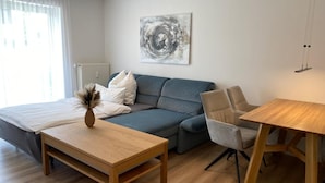 A modern living room with a sofa, a small wooden table, a chair, and a hanging light fixture. - Mountain idyll -renovated and high quality with solid wood bed at comfort height (Altenberg)