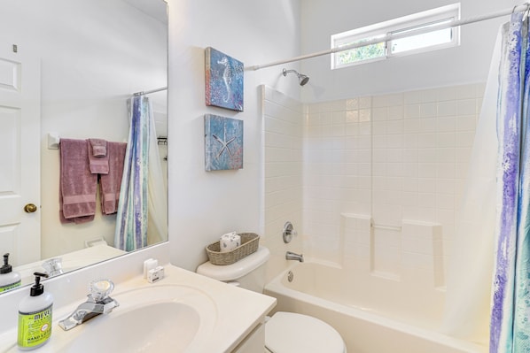 Ein Badezimmer mit Waschbecken, Toilette und Badewanne. Handtücher hängen an der Wand und über der Badewanne befindet sich ein Fenster.