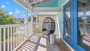 A covered porch with a white railing, a wicker chair, and a small round table.