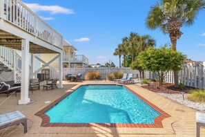 A rectangular swimming pool with a brick border, surrounded by a patio area with lounge chairs and a covered seating area. - Seafoam Beautiful 3BR Home With Heated Private Pool - 4 Min Walk to Beach! (Panama City Beach)
