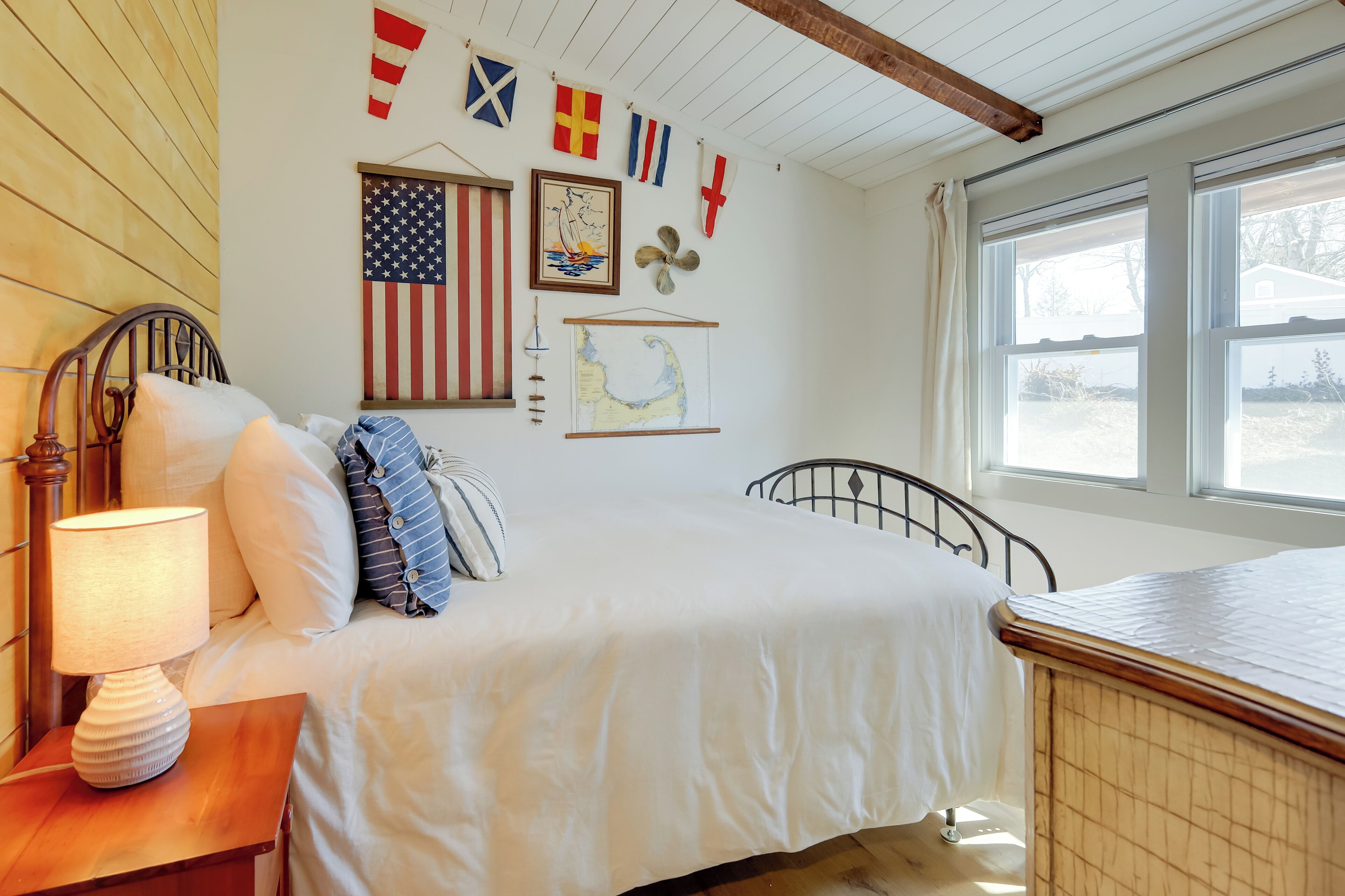 A neatly arranged bedroom with a bed, bedside table, lamp, and various wall decorations including flags and a map.