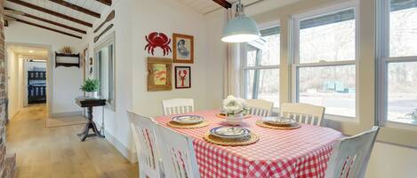 Un coin repas avec une nappe à carreaux, des chaises blanches et un luminaire suspendu.