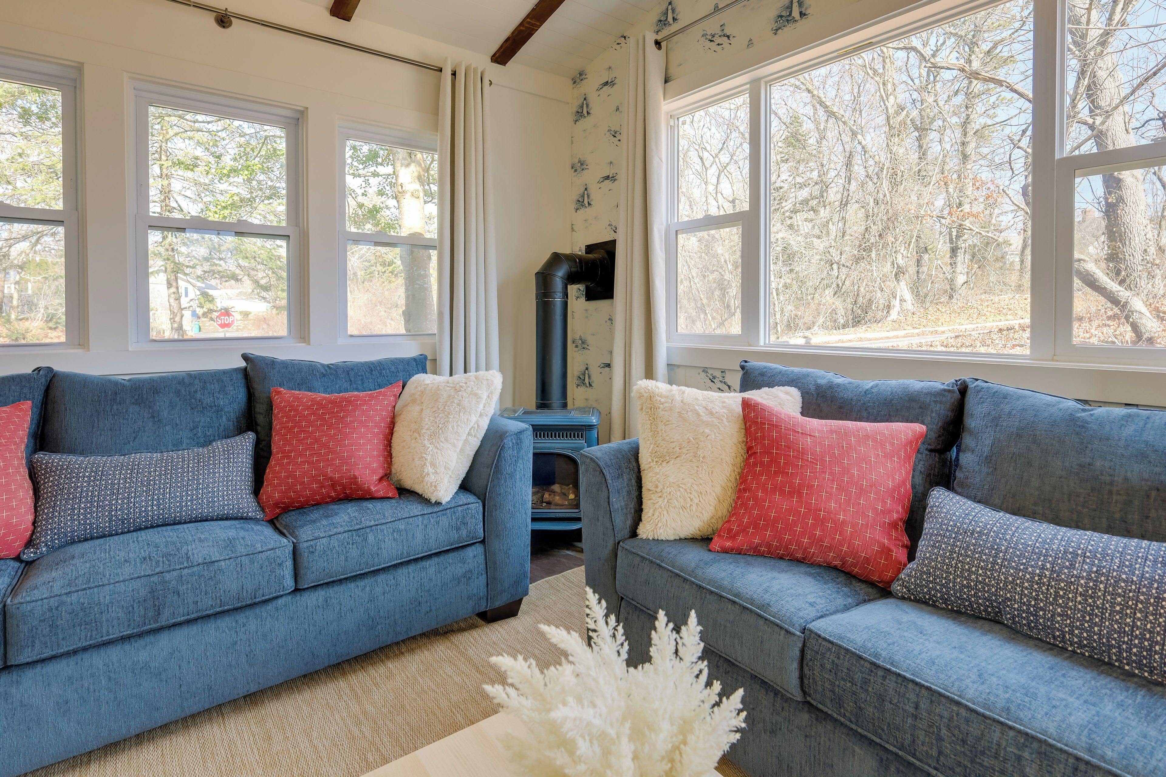 A living room with two sofas, a fireplace, and large windows with a view of trees.