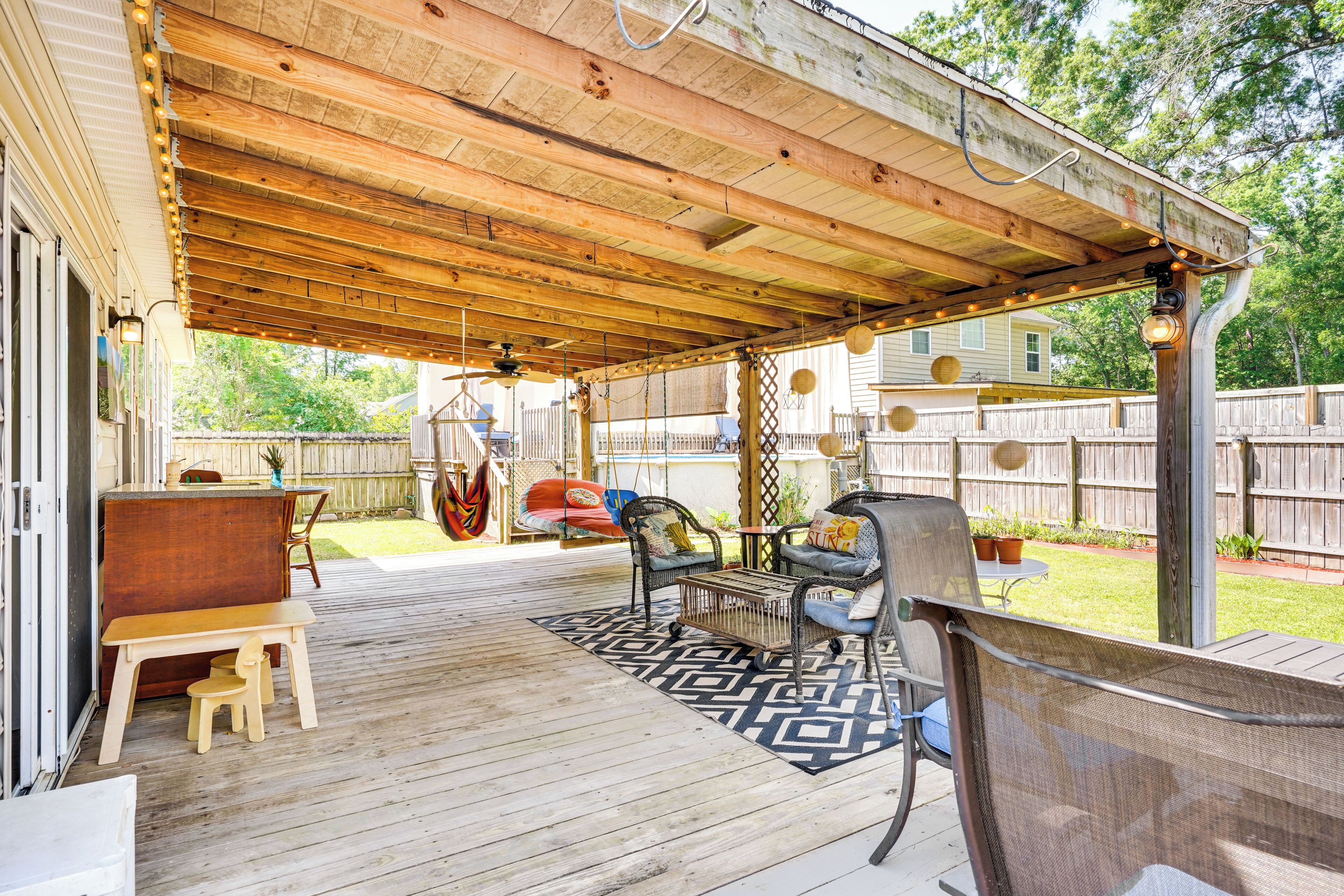 Une terrasse couverte avec une plateforme en bois, des sièges d’extérieur et une balançoire suspendue.