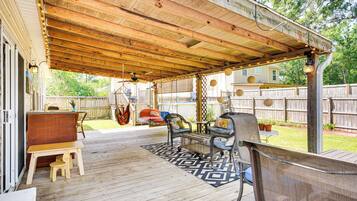 Une terrasse couverte avec une plateforme en bois, des sièges d’extérieur et une balançoire suspendue.
