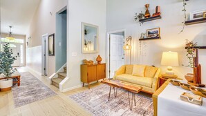 Een ruime woonkamer met een bank, salontafel en decoratieve objecten. Een trap leidt naar een andere kamer, en er is een deur aan de rechterkant.