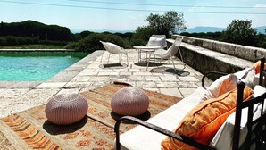 Un espace aménagé au bord de la piscine, avec des chaises longues, une table et deux petits bancs ronds.